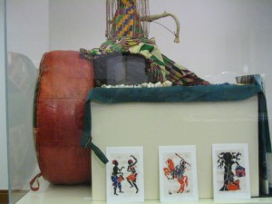 mall representation of a Chief’s cushion (left) Small drum (above left) ~Courtesy loan from Ligali Harruna Woodblock prints on cloth made into cards (above) Dress and head wrap (above) Bead and shell necklaces made by village women (above) ~Courtesy Loan from Victoria Abioye-Oyewusi